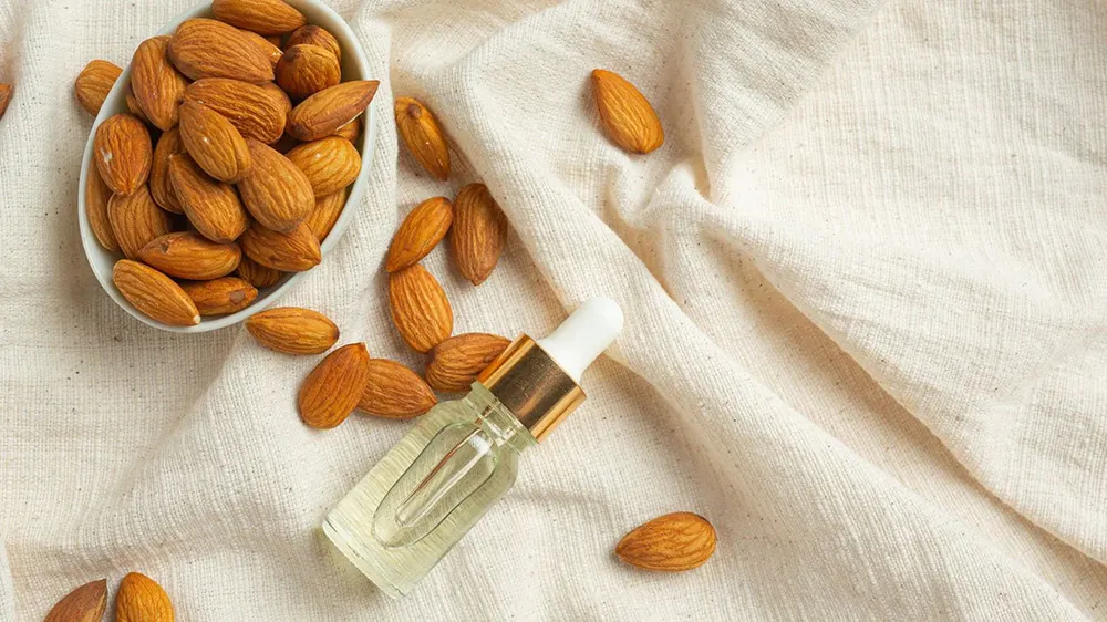 بهترین روغن برای از بین بردن چین و چروک صورت 5 یک ظرف بادام درختی و یک شیشه روغن بادام کنار آن
