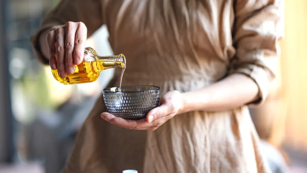 زدن روغن زیتون به صورت قبل از خواب چه فایدهای دارد؟ 12 زنی درحال ریختن روغن زیتون داخل یک کاسه